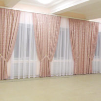 Простой дизайн и крсивый эффект дают розово-коралловые шторы в зале с большим количеством окон